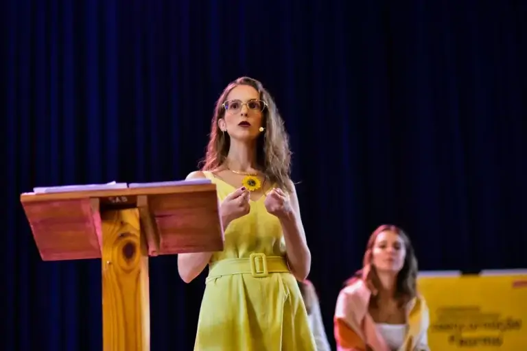 Imagem de Mariana Azoubel no palco durante palestra sobre terapias naturais e medicina antroposófica, promovendo bem-estar integral.